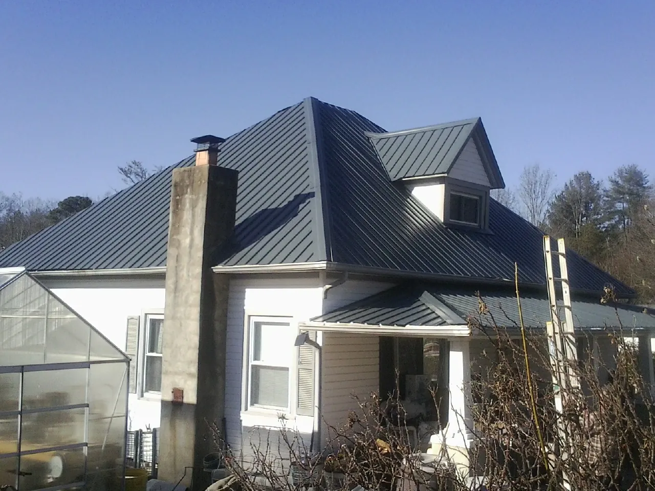 Dark blue standing seam metal roof on a white farmhouse with dormer — Slate & Tile Roof Repair by Roofing Brothers in Michigan Center