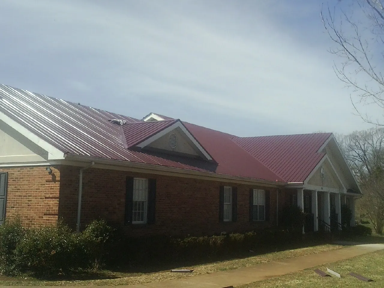 Red metal roof with gabled entries on a long brick building, from a Hail Damage Roof Repair job in Michigan Center