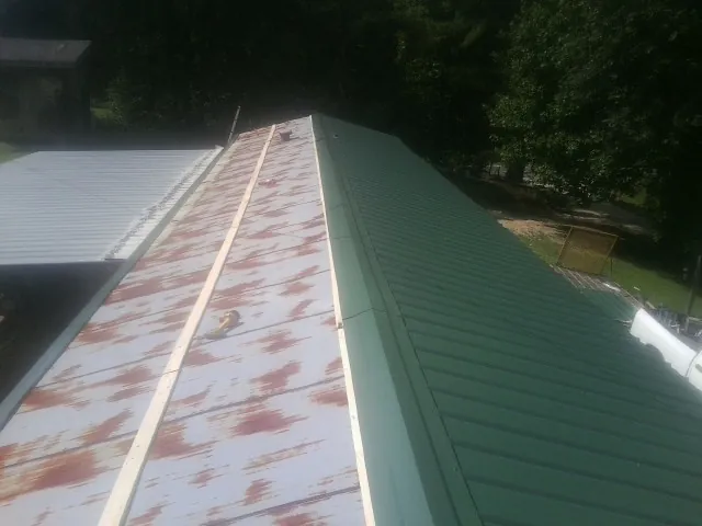 Old rusted panels beside newly installed green metal roofing — Wind Damage Roof Repair by Roofing Brothers in Michigan Center