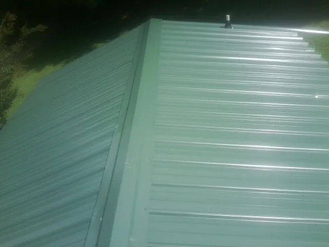 New green metal panels meeting at the ridge of a roof — Flat Roof Repair work by our crew in Michigan Center