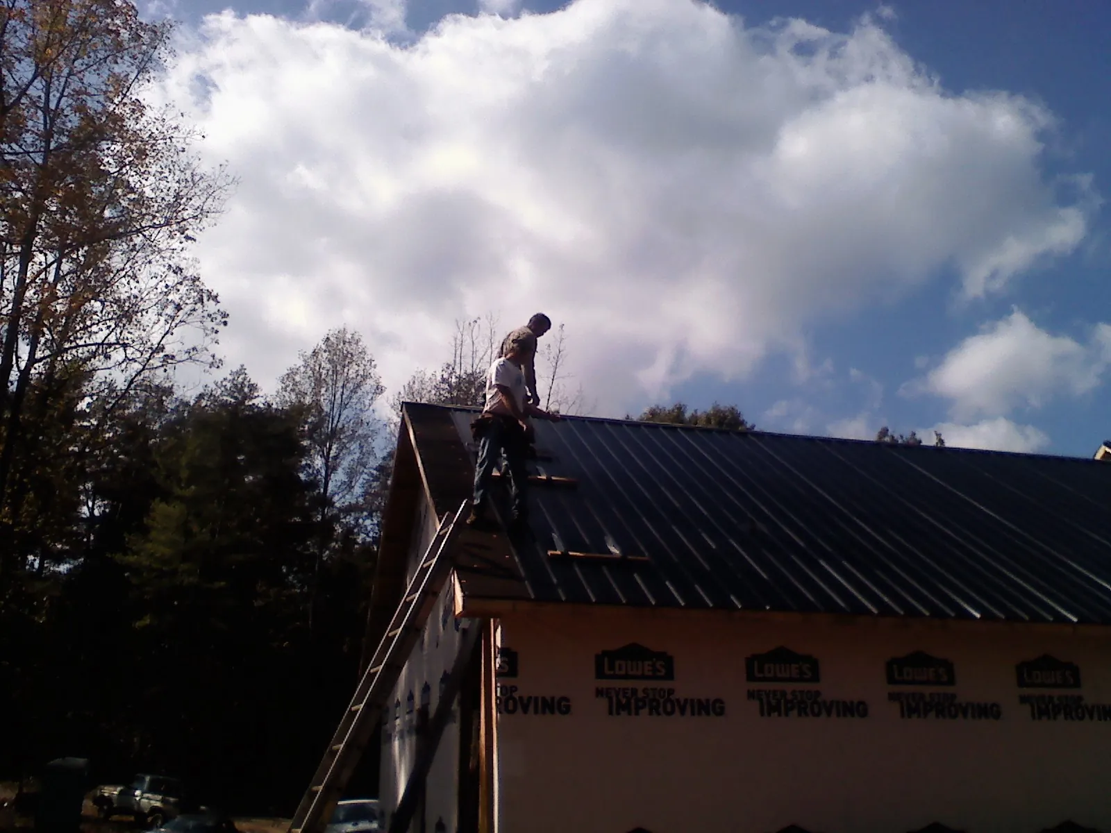 Roofer fastening dark metal panels high against a cloudy sky, from a Roof Inspection job in Michigan Center
