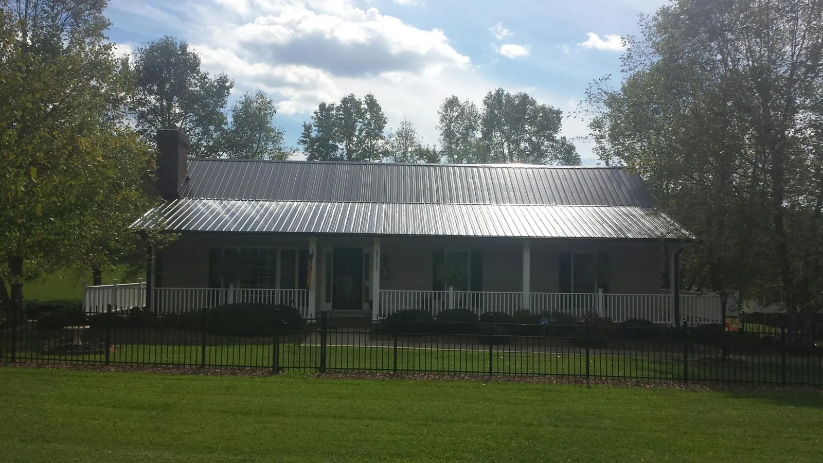 Gray metal roof on a brick ranch with a full width front porch — Gutter Guard Installation work by our crew in Michigan Center