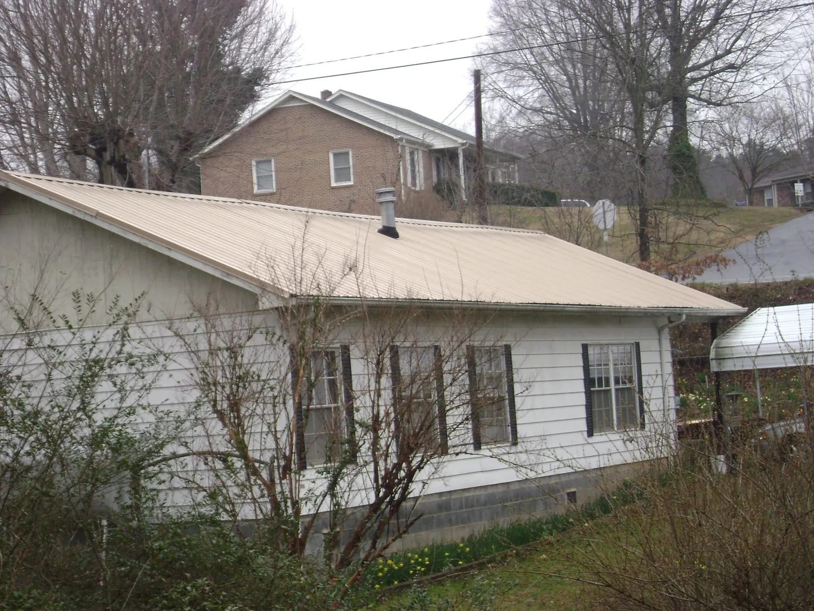 Tan metal roof on a white sided house set into a hillside — Commercial Roofing by Roofing Brothers in Michigan Center