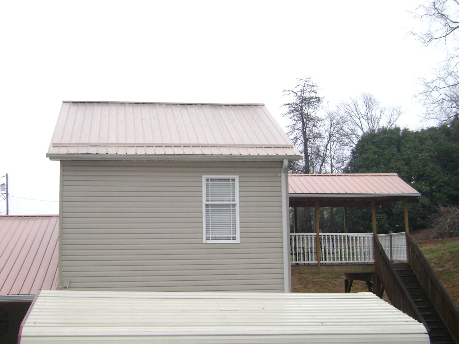Tan metal roofs on a two story addition and attached porch, from a Roof Replacement job in Michigan Center